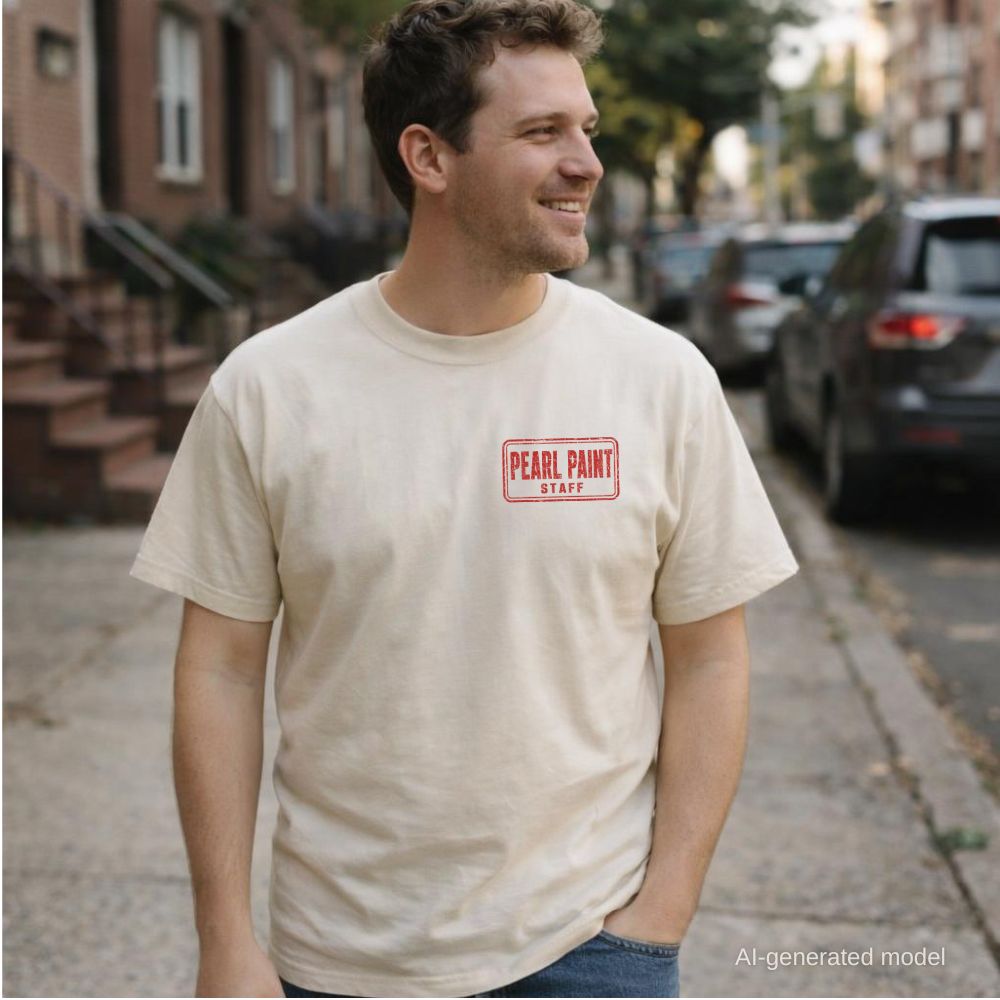 A man wearing an ivory Comfort Colors T-shirt with red Pearl Paint NYC small front chest print, while standing on a NYC street.