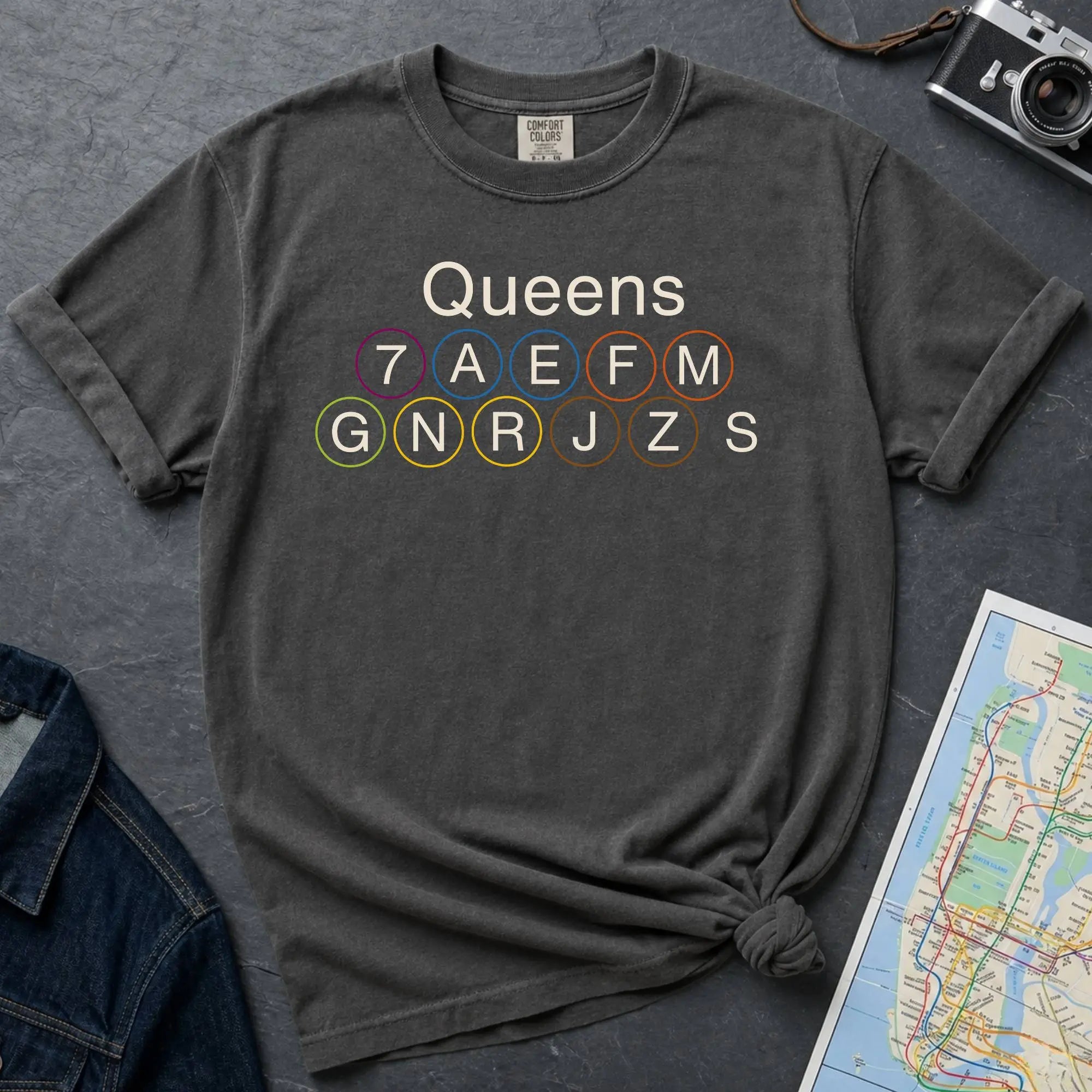 Pepper colored Comfort Colors t-shirt featuring a minimalist Queens subway line graphic with Queens text and classic NYC train icons.