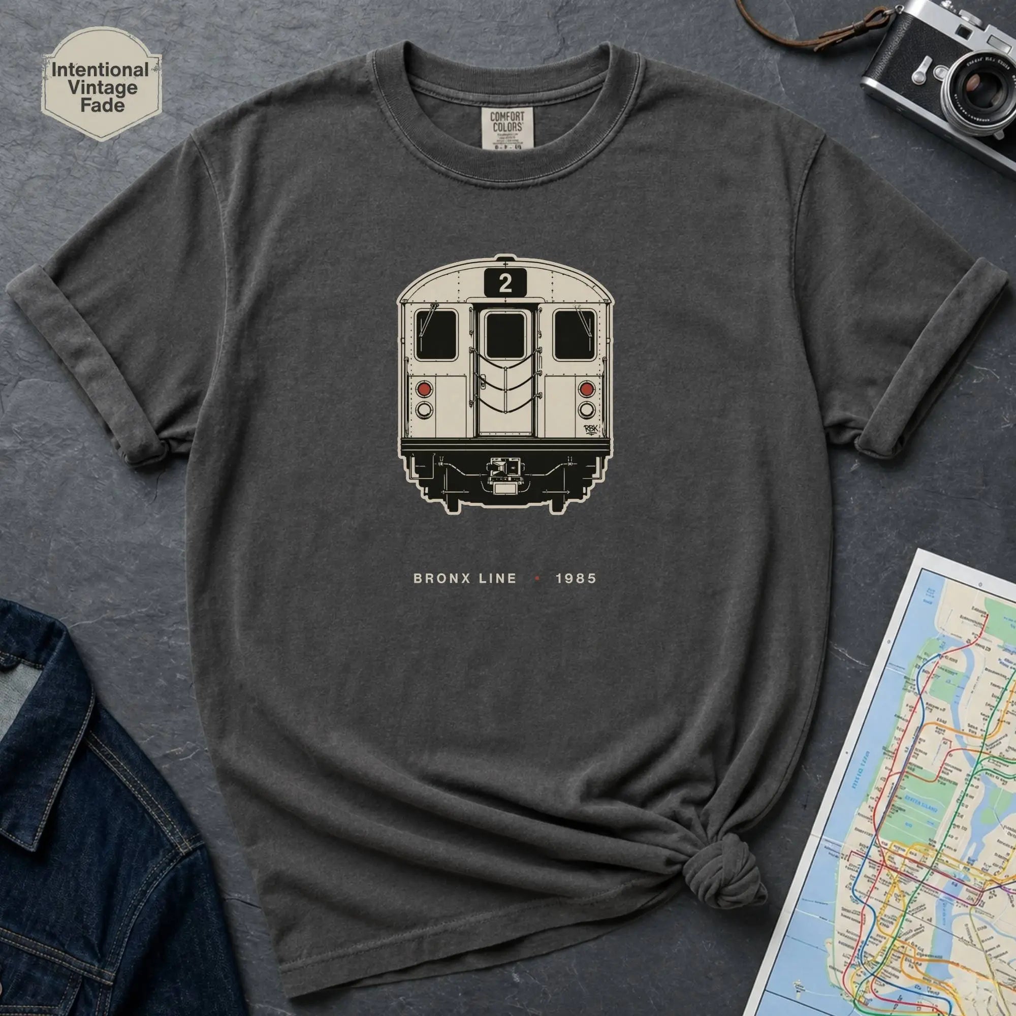 Pepper colored t-shirt with a NYC subway train graphic on a dark surface with a map and a denim jacket.