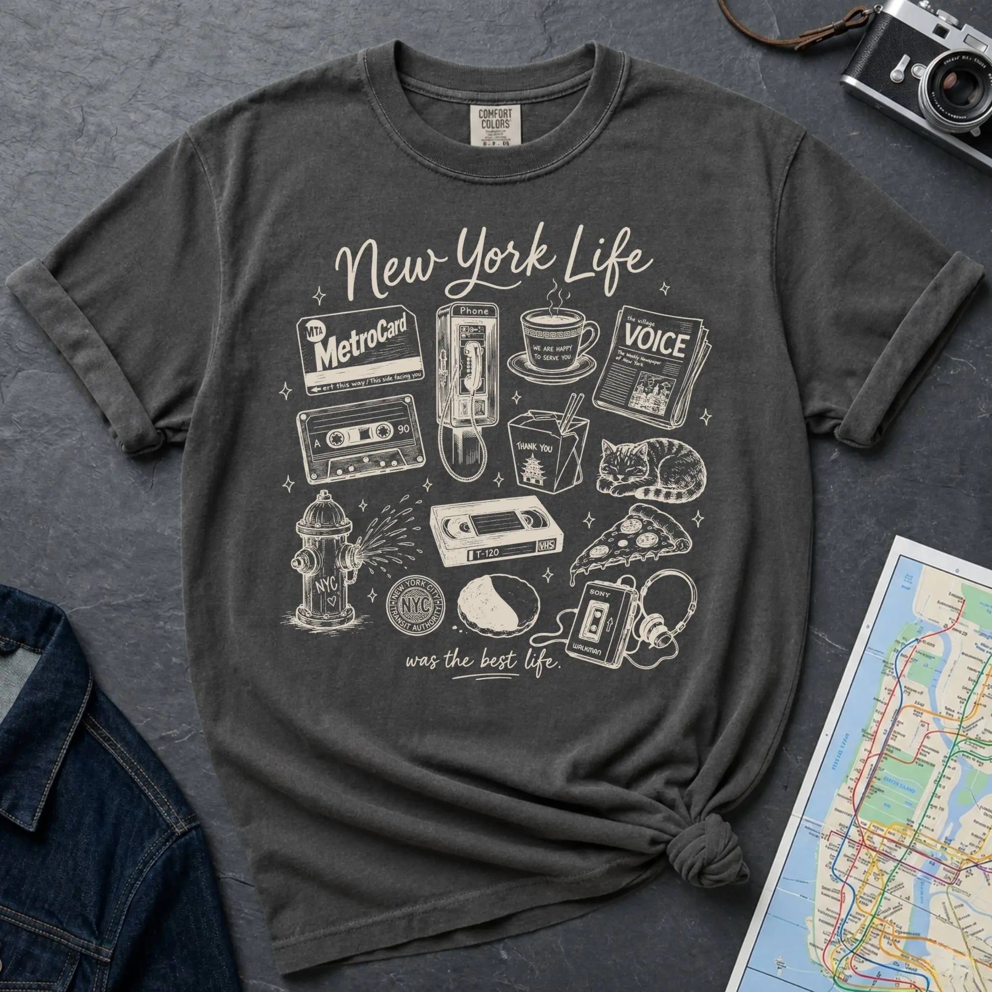 Pepper colored Comfort Colors t-shirt featuring a New York Life Was the Best Life graphic with hand-drawn NYC nostalgia icons including a MetroCard, cassette tape, pay phone, coffee cup, newspaper, pizza slice, fire hydrant, Walkman, and bodega cat.
