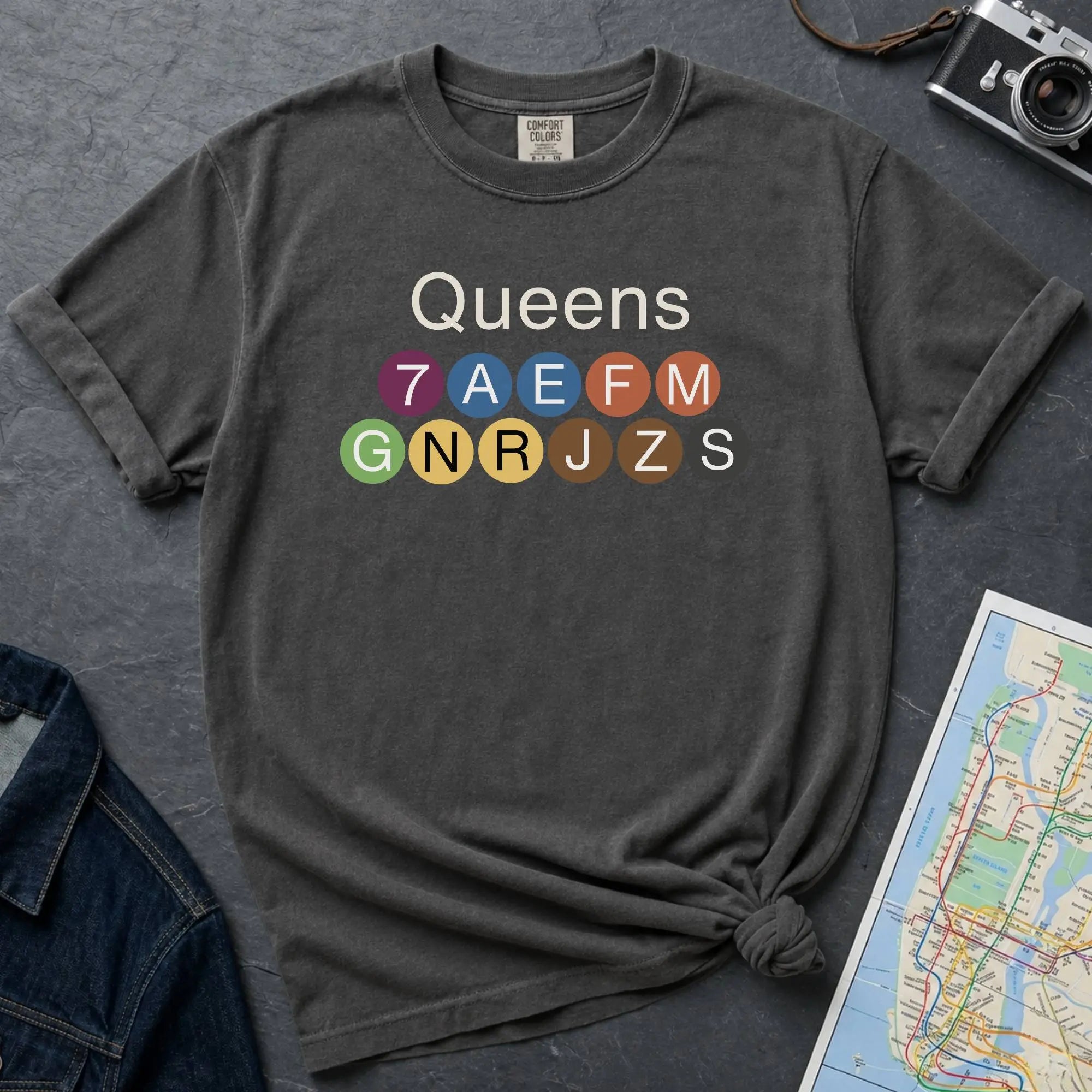 Pepper colored Black Comfort Colors t-shirt featuring a minimalist Queens subway line graphic with colorful NYC train icons.