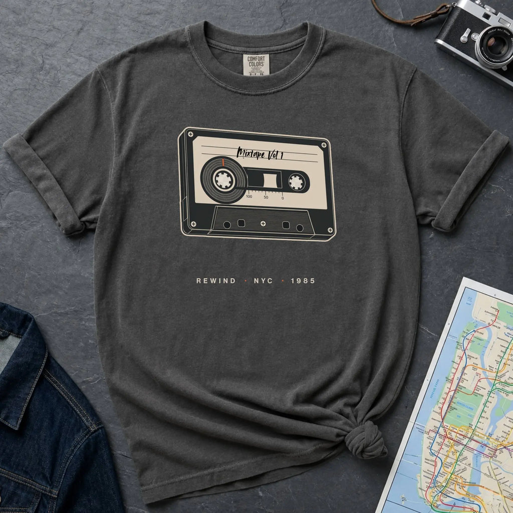 Pepper colored t-shirt with cassette tape graphic and text on a gray surface with denim jacket and map.