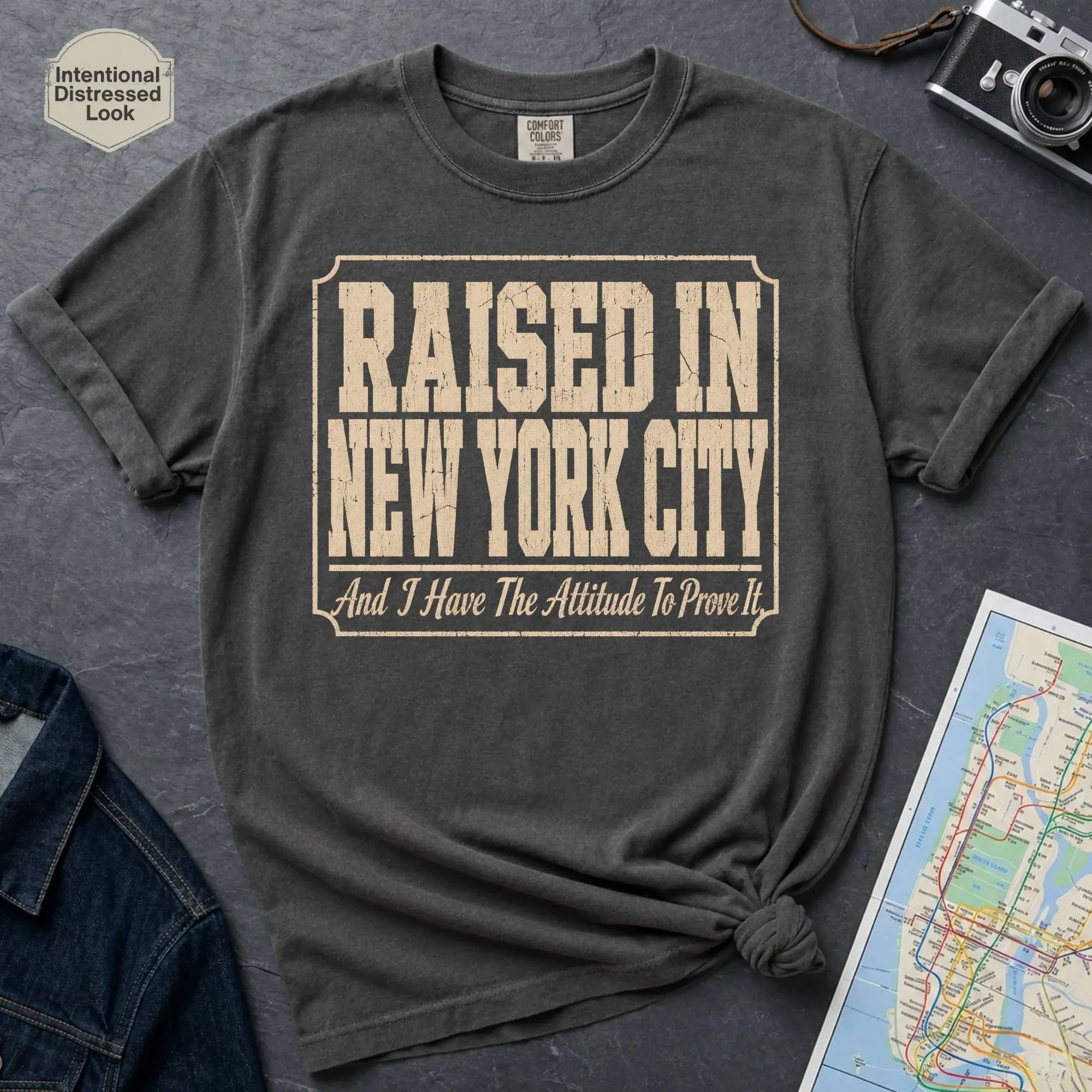 Pepper colored Comfort Colors t-shirt featuring distressed vintage text that reads “Raised in New York City, And I Have the Attitude to Prove It.