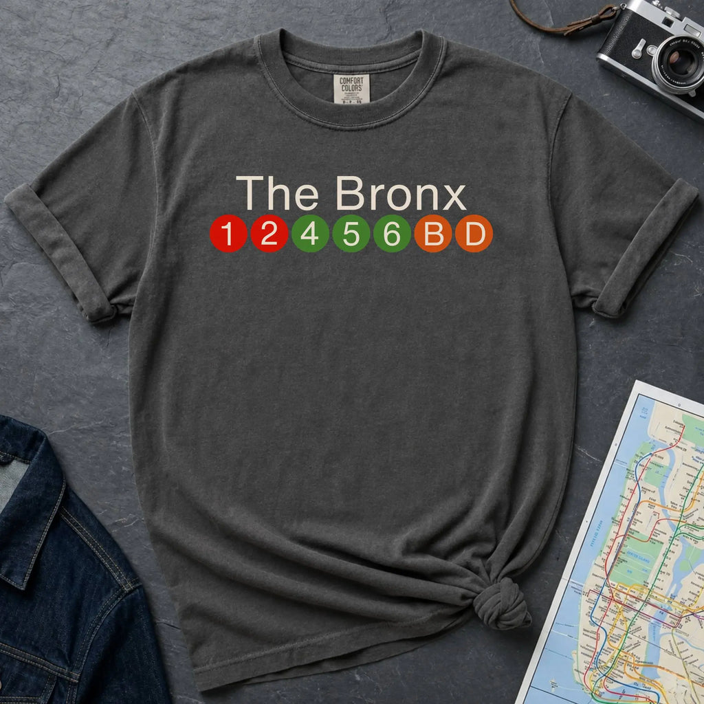Pepper colored Comfort Colors t-shirt featuring a minimalist Bronx subway line graphic with The Bronx text and colorful NYC train icons.