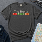 Pepper colored Comfort Colors t-shirt featuring a minimalist Bronx subway line graphic with The Bronx text and colorful NYC train icons.