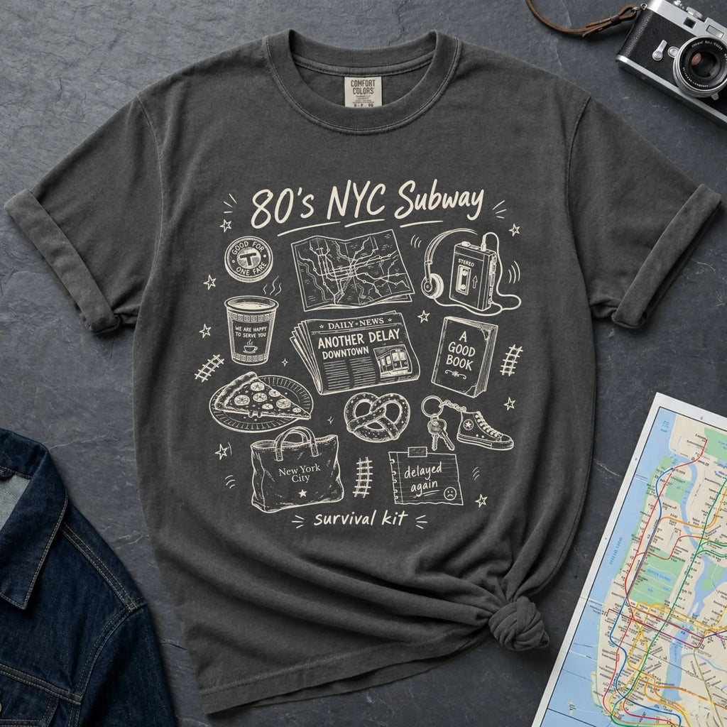 Pepper colored t-shirt with '80s NYC Subway Survival Kit' graphic design on a dark surface with a map and denim jacket.