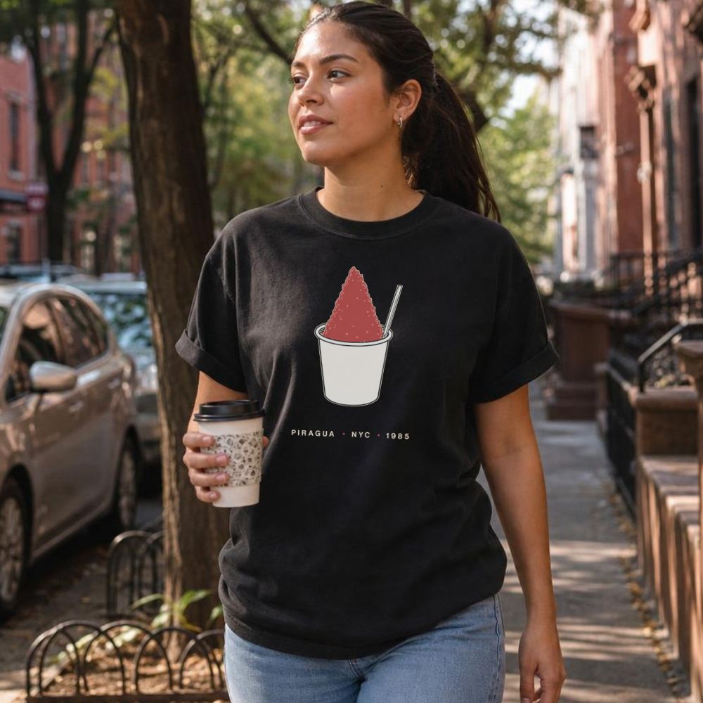 Woman wearing a blackComfort Colors t-shirt with a piragua graphic and text, walking on a city street.