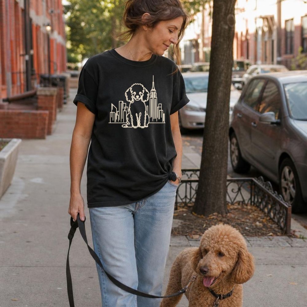 Woman walking a Poodle on a city street wearing a black Comfort Colors t-shirt with a Poodle and cityscape design.