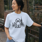 Woman wearing a Light Blue colored Comfort Colors t-shirt with a poodle and cityscape design outdoors.