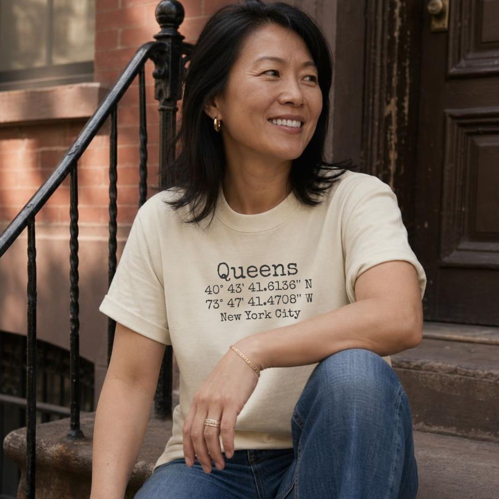 Woman wearing an Ivory Comfort Colors 'Queens' t-shirt with coordinates, sitting on a stoop.