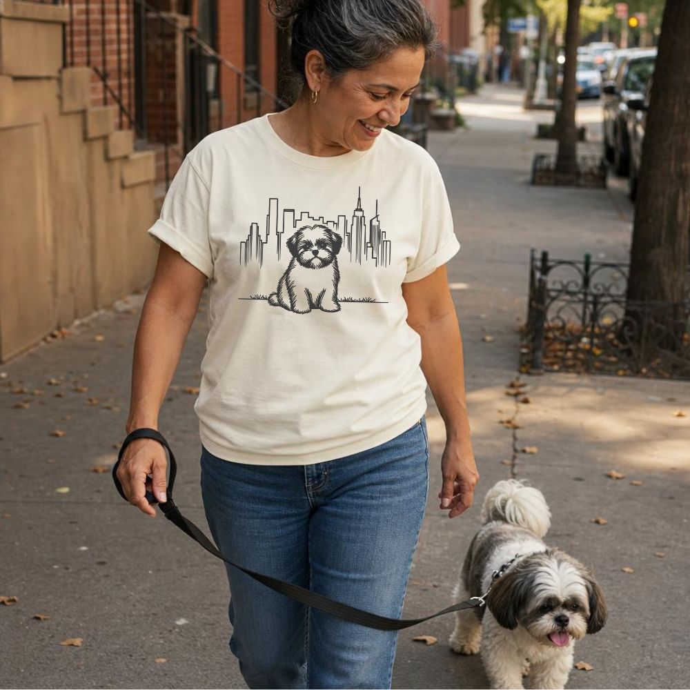 Woman walking a Shih Tzu on a leash in an urban setting, wearing an Ivory Comfort Colors t-shirt with the same dog and cityscape design.