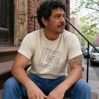 Man sitting on a stoop wearing an Ivory Comfort Colors t-shirt with New York City skelzies design.