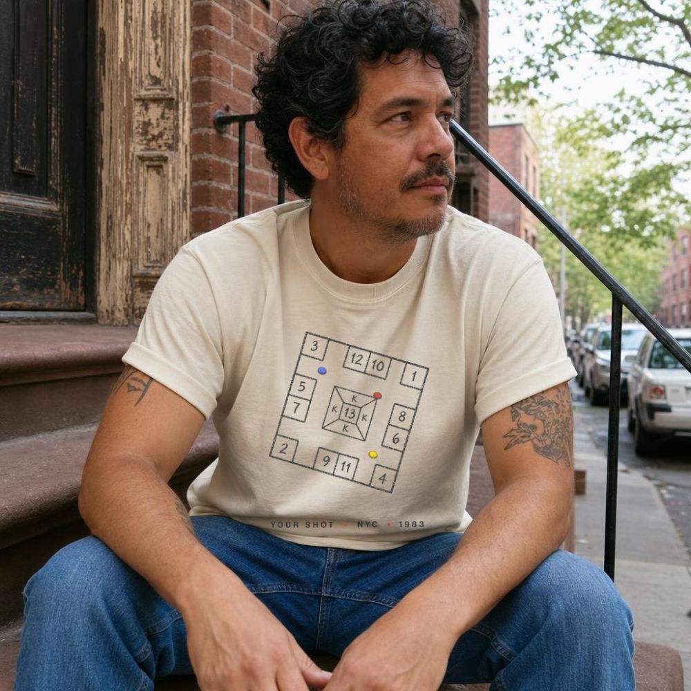 Man sitting on a stoop wearing an Ivory Comfort Colors t-shirt with New York City skelzies design.