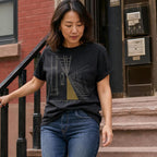 Woman wearing a black Comfort Colors t-shirt with a graphic design of a person on train tracks, standing on steps in an urban setting.