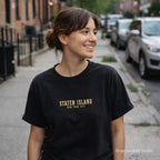 Woman wearing a black Comfort Colors t-shirt with 'Staten Island, New York City' text on a street.