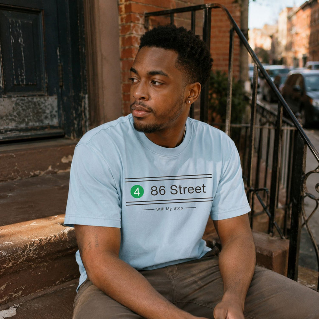 Man wearing a Light blue t-shirt with '86 Street' design sitting on a stoop.