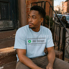 Man wearing a Light blue t-shirt with '86 Street' design sitting on a stoop.