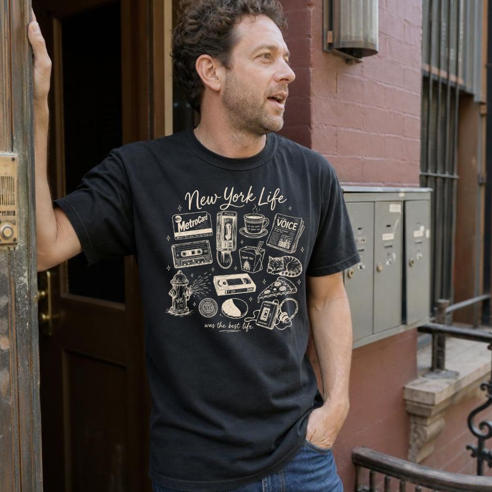 Man wearing a black t-shirt with 'New York Life' graphic design, standing on a street.