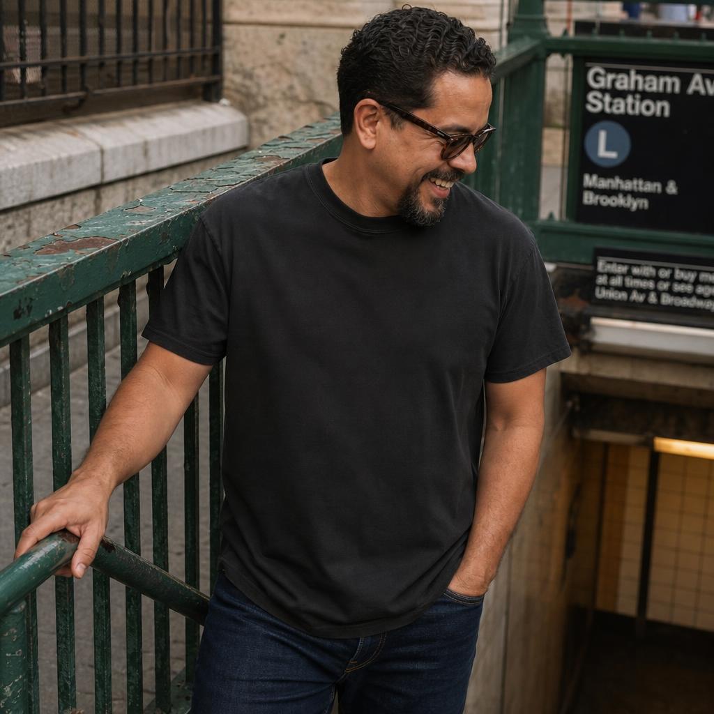 Man in a black Comfort Colors t-shirt with 'Brooklyn' and coordinates printed on it, standing at a subway station
