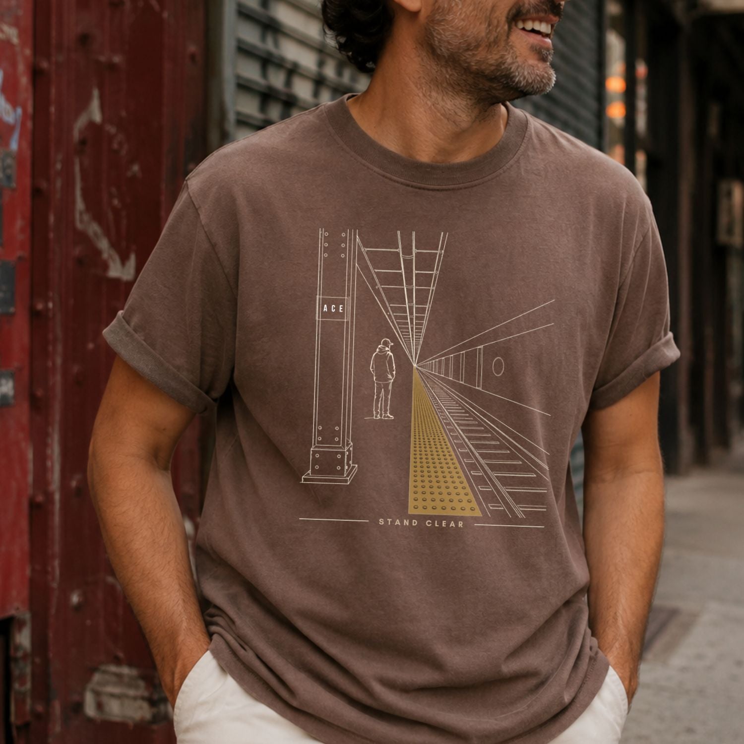 Man wearing an Espresso colored Comfort Colors t-shirt with a graphic design of a subway platform and person.