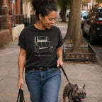 Woman walking a dog on a leash in an urban setting, wearing a Black t-shirt with a graphic design of a train seat and text.