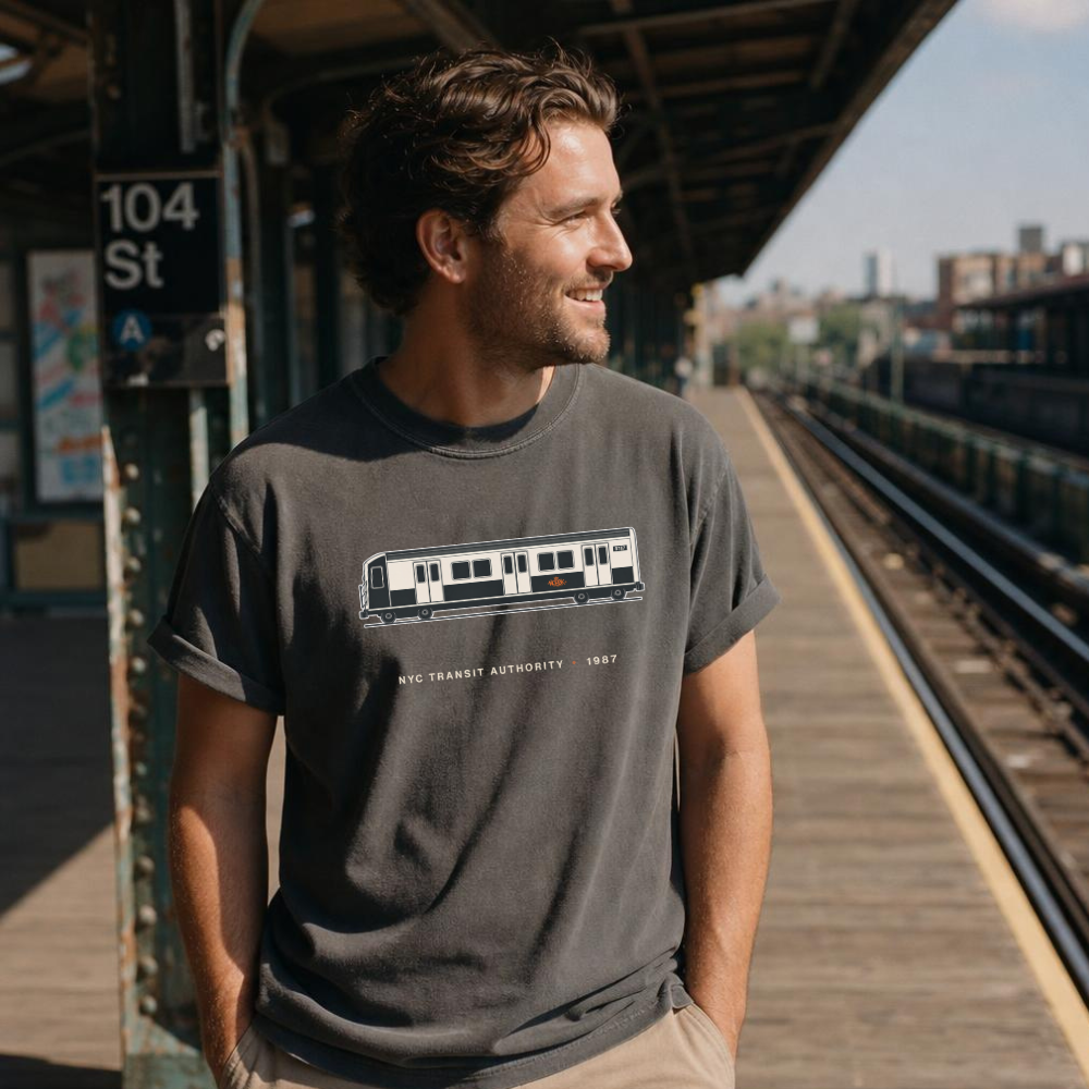 Man wearing a t-shirt with a train design on a NYC subway platform.
