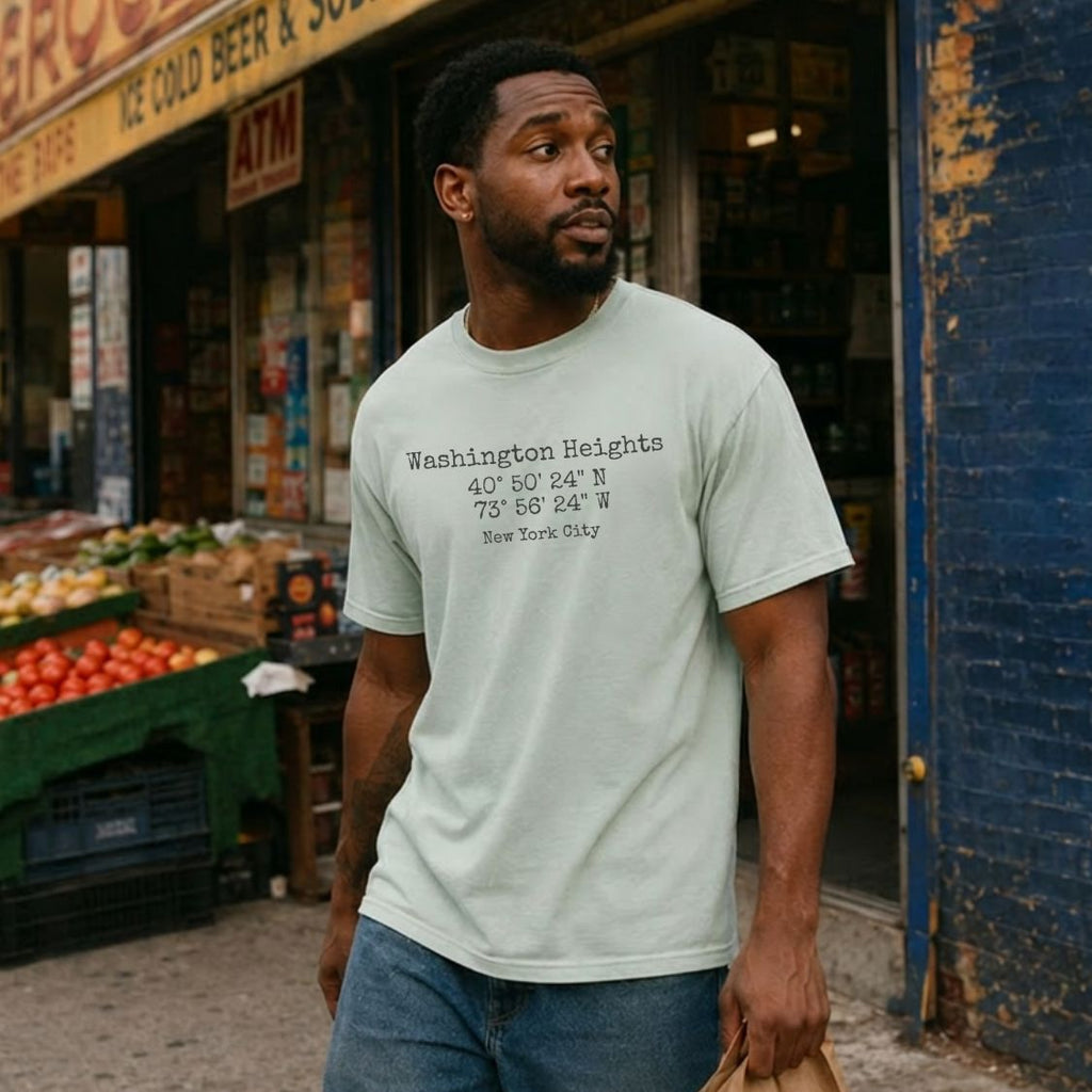 Man wearing a Bay colored Comfort Colors t-shirt with 'Washington Heights' text with coordinates and 'New York City' in front of a store