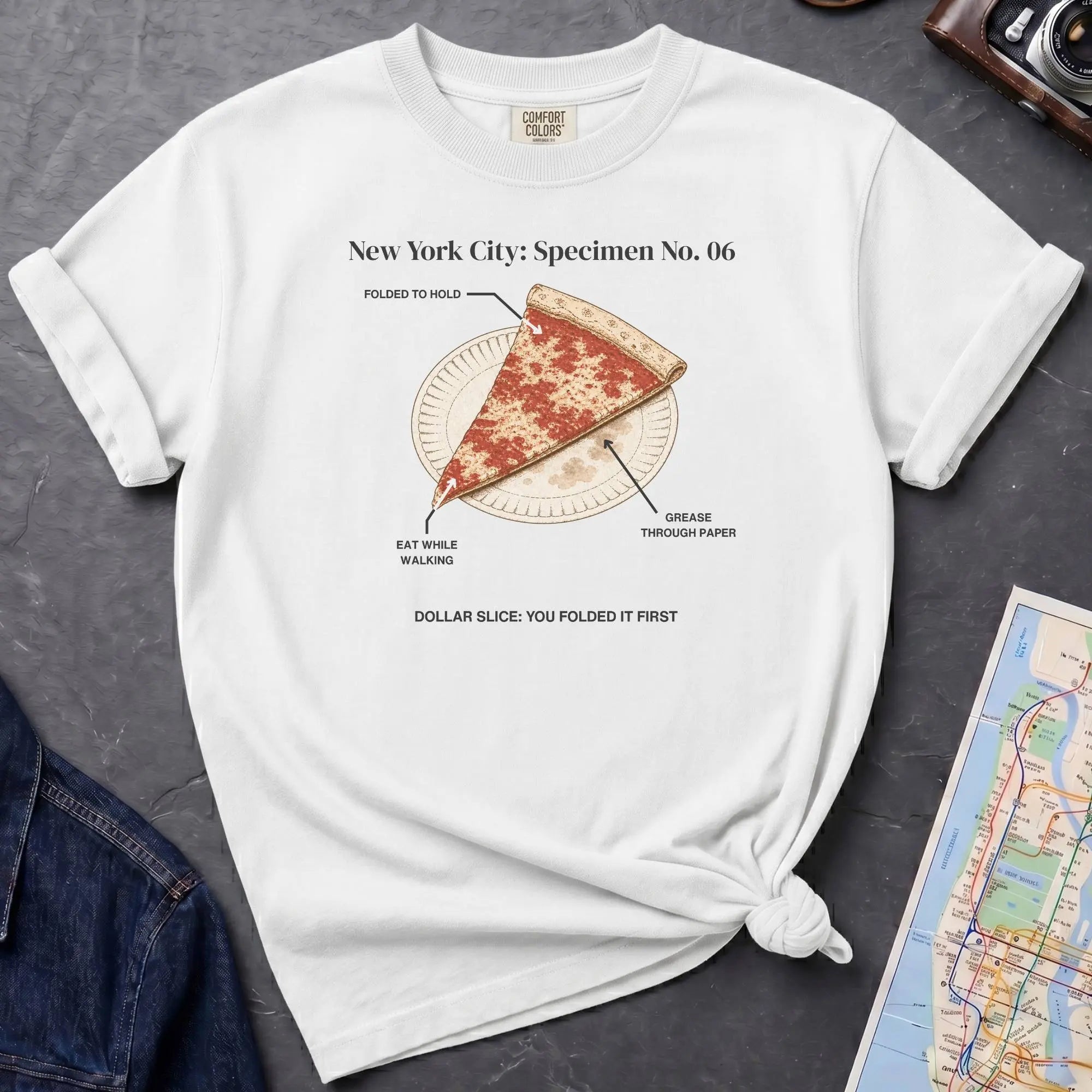 White Comfort Colors t-shirt featuring a vintage New York City dollar slice pizza graphic with specimen-style callouts and a folded slice on a paper plate.