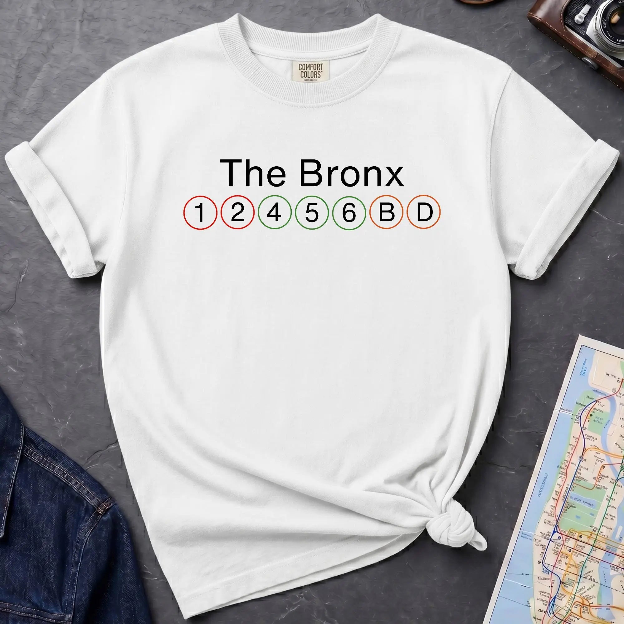 White Comfort Colors t-shirt featuring a minimalist Bronx subway line graphic with The Bronx text and classic NYC train icons.