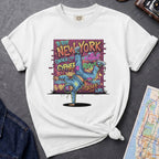 White t-shirt with a colorful graphic design featuring a breakdancer and text on a dark surface with a denim jacket and a map.