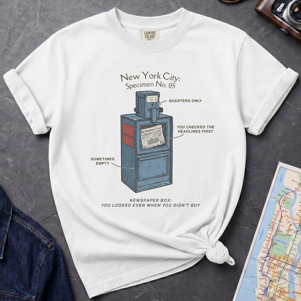 White t-shirt with a graphic design of a newspaper box on a dark surface with a map and jacket.