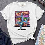 White t-shirt with a colorful graphic design featuring a breakdancer and text on a dark surface with a denim jacket and a map.