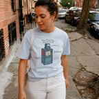 Woman wearing a Light blue Comfort Colors t-shirt with a New York City newspaper box design on a city street.